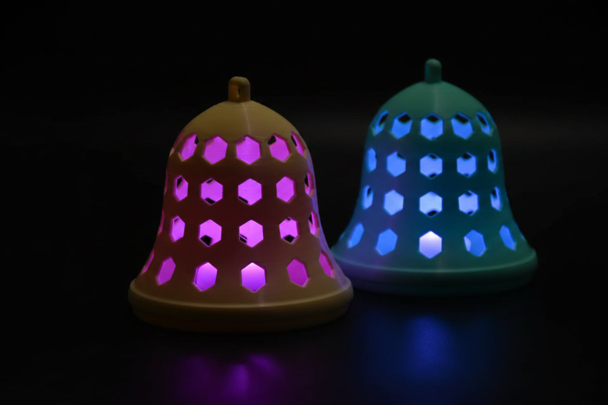 3D printed hexagon cutout holiday bell ornaments in teal and cream on a wood surface