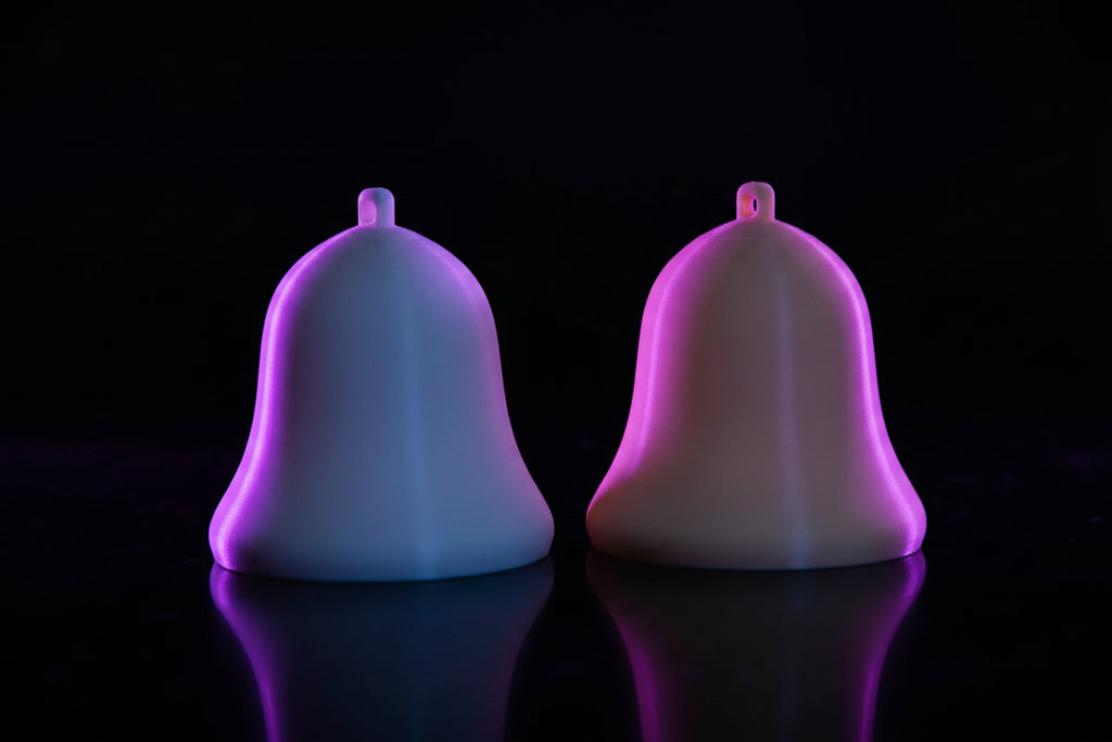 3D printed solid holiday bell ornaments in white and cream on a wood surface