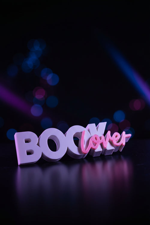 3D printed Book Lover sign in white and pink script lying flat with dried flowers