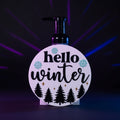 3D printed Hello Winter BBW interchangeable soap cover with raised black text, icy blue snowflakes, gold stars, and pine trees on white round base - front view on foaming dispenser